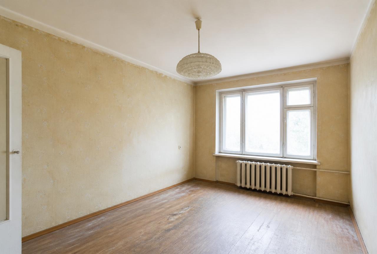 Wohnzimmer vor der Renovierung mit vergilbter Tapete und abgenutztem Boden